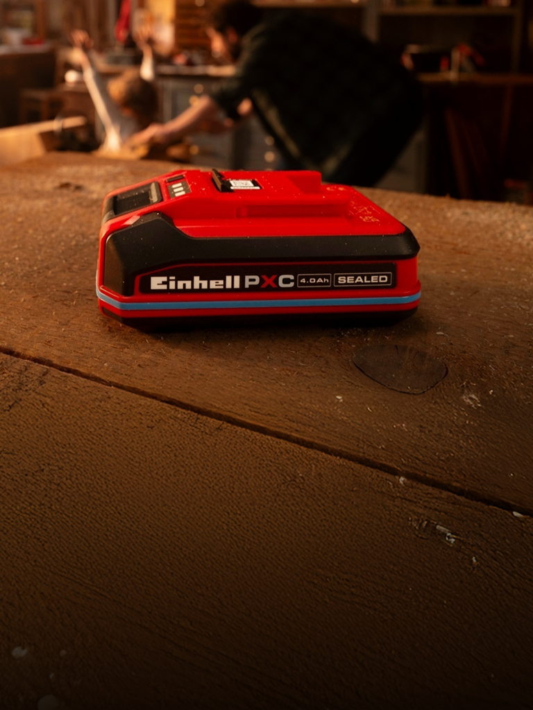 Μπαταρία Einhell Power X-Change 4.0Ah SEALEAD σε ξύλινο πάγκο εργασίας, με μπλε δακτύλιο και ετικέτα.