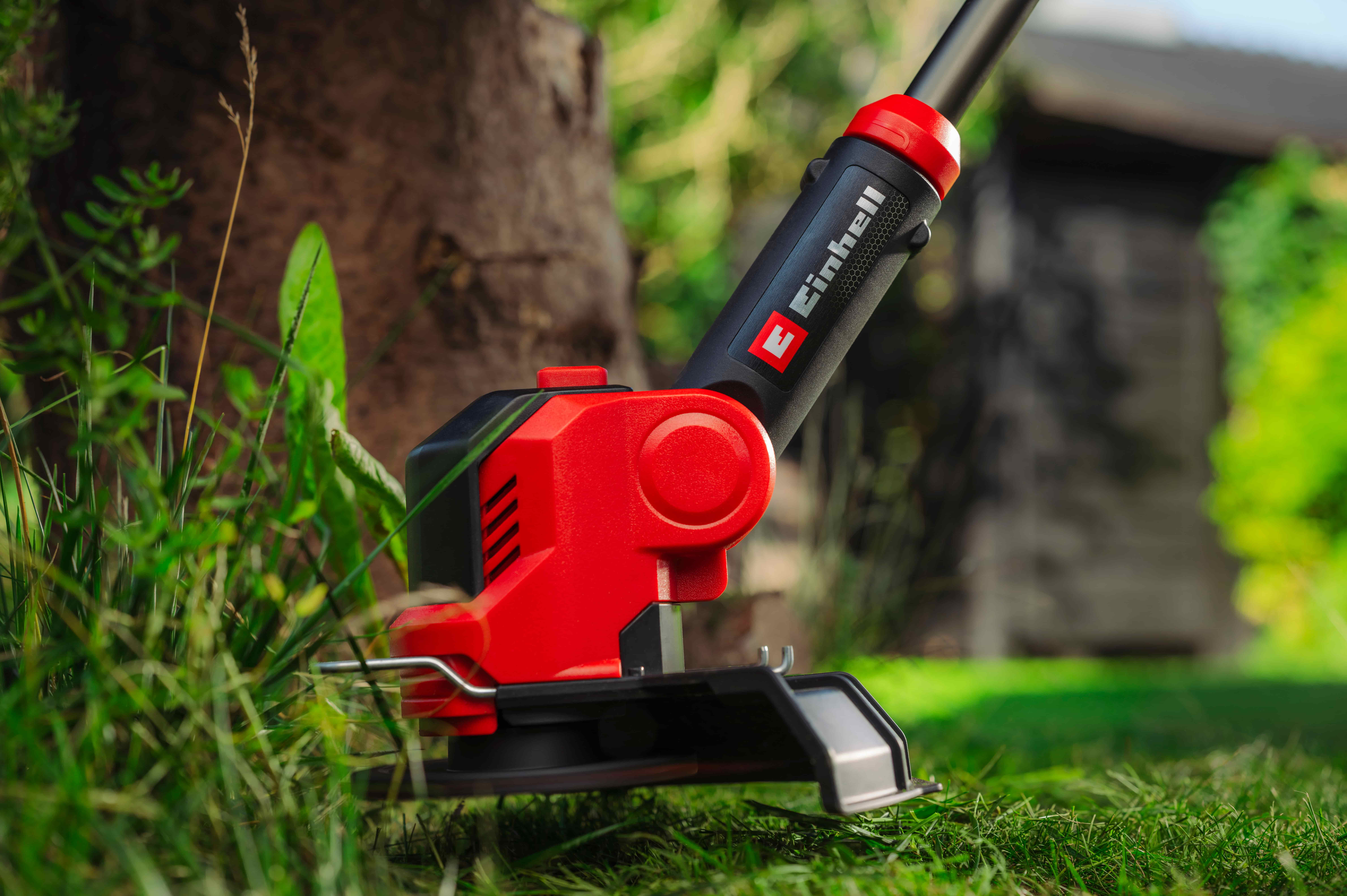 Τρίμερ Einhell κόβει το γρασίδι γύρω από δέντρο στον κήπο.