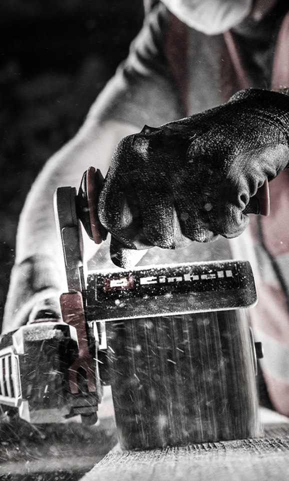 A person wearing black gloves sands a piece of wood using a red Einhell sander, with dust particles flying in the air.