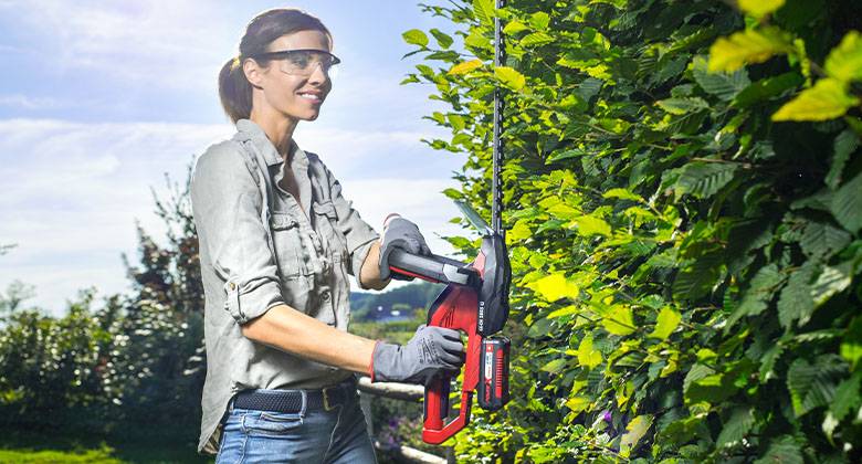 woman cutting hedge with cordless hedge trimmer